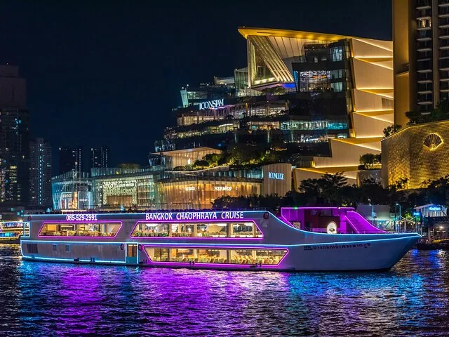 Beleuchtetes Dinner-Kreuzfahrtschiff, das nachts vor ICONSIAM fährt.
