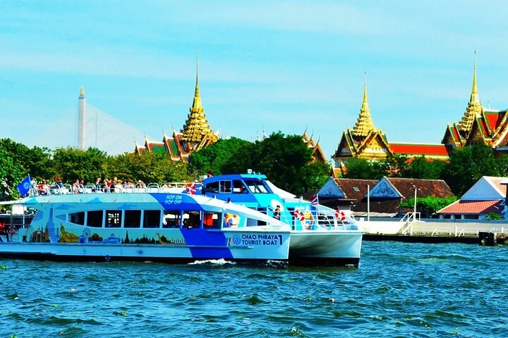Ein blau-weißes Touristenboot auf dem Fluss mit Tempeln im Hintergrund.